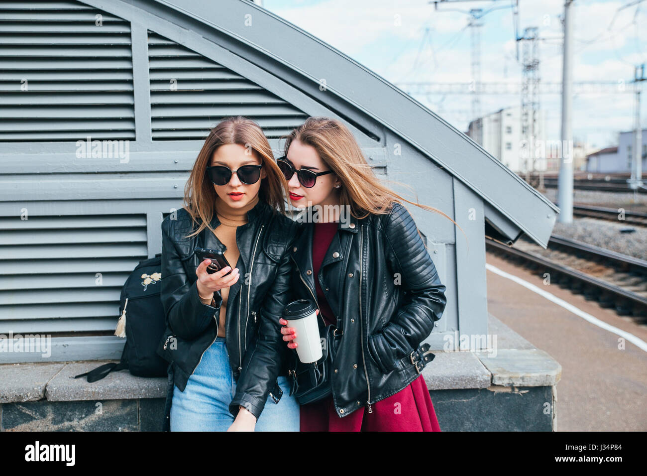 Conversazione tra due donne nella città.Outdoor Lifestyle ritratto di due migliori amici hipster ragazze indossano Elegante giacca di pelle e occhiali da sole con caffè, going crazy e avente un grande tempo insieme Foto Stock