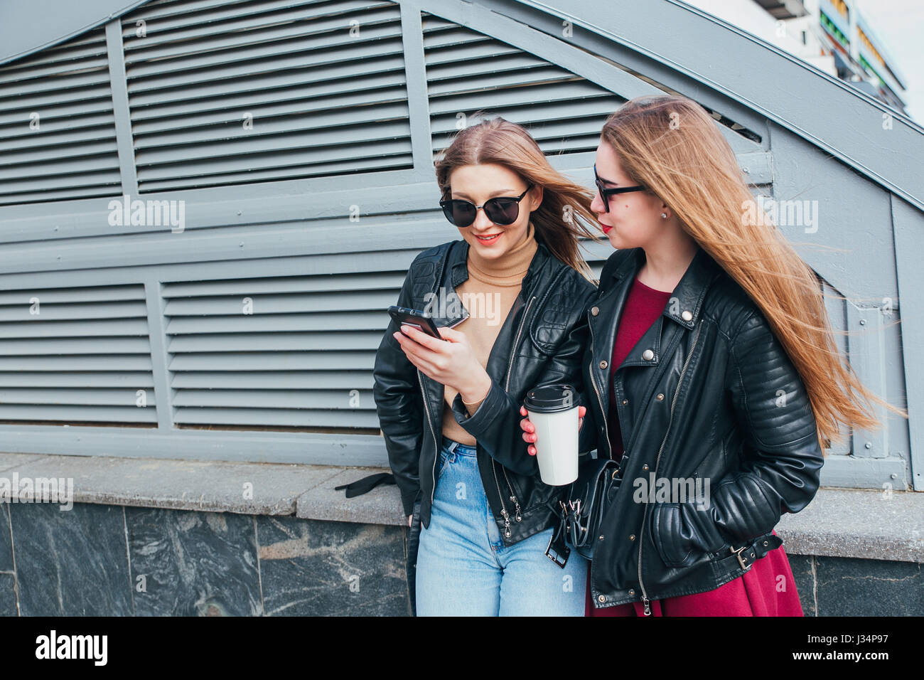 Conversazione tra due donne nella città.Outdoor Lifestyle ritratto di due migliori amici hipster ragazze indossano Elegante giacca di pelle e occhiali da sole con caffè, going crazy e avente un grande tempo insieme Foto Stock