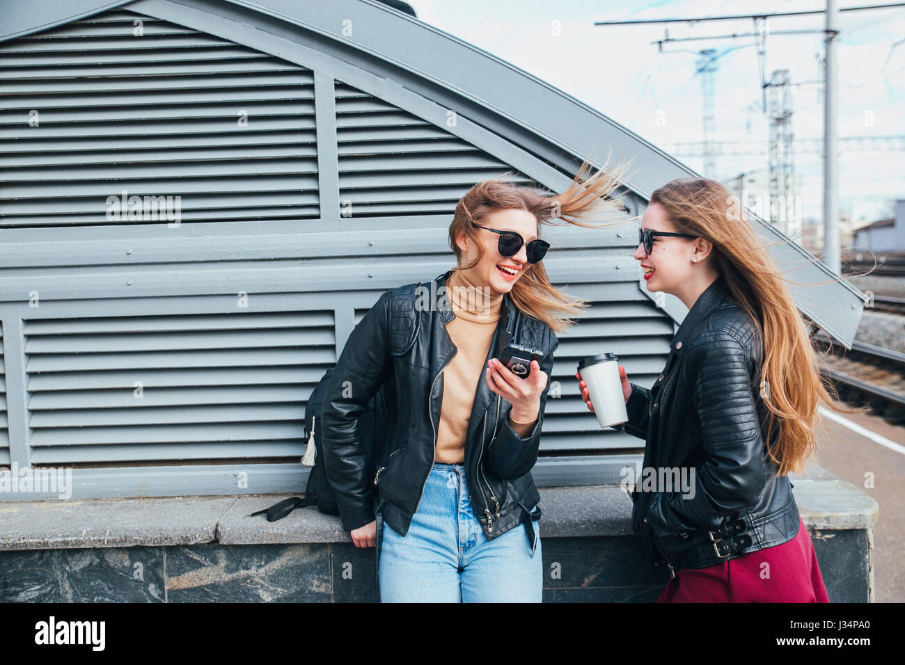 Conversazione tra due donne nella città.Outdoor Lifestyle ritratto di due migliori amici hipster ragazze indossano Elegante giacca di pelle e occhiali da sole con caffè, going crazy e avente un grande tempo insieme Foto Stock