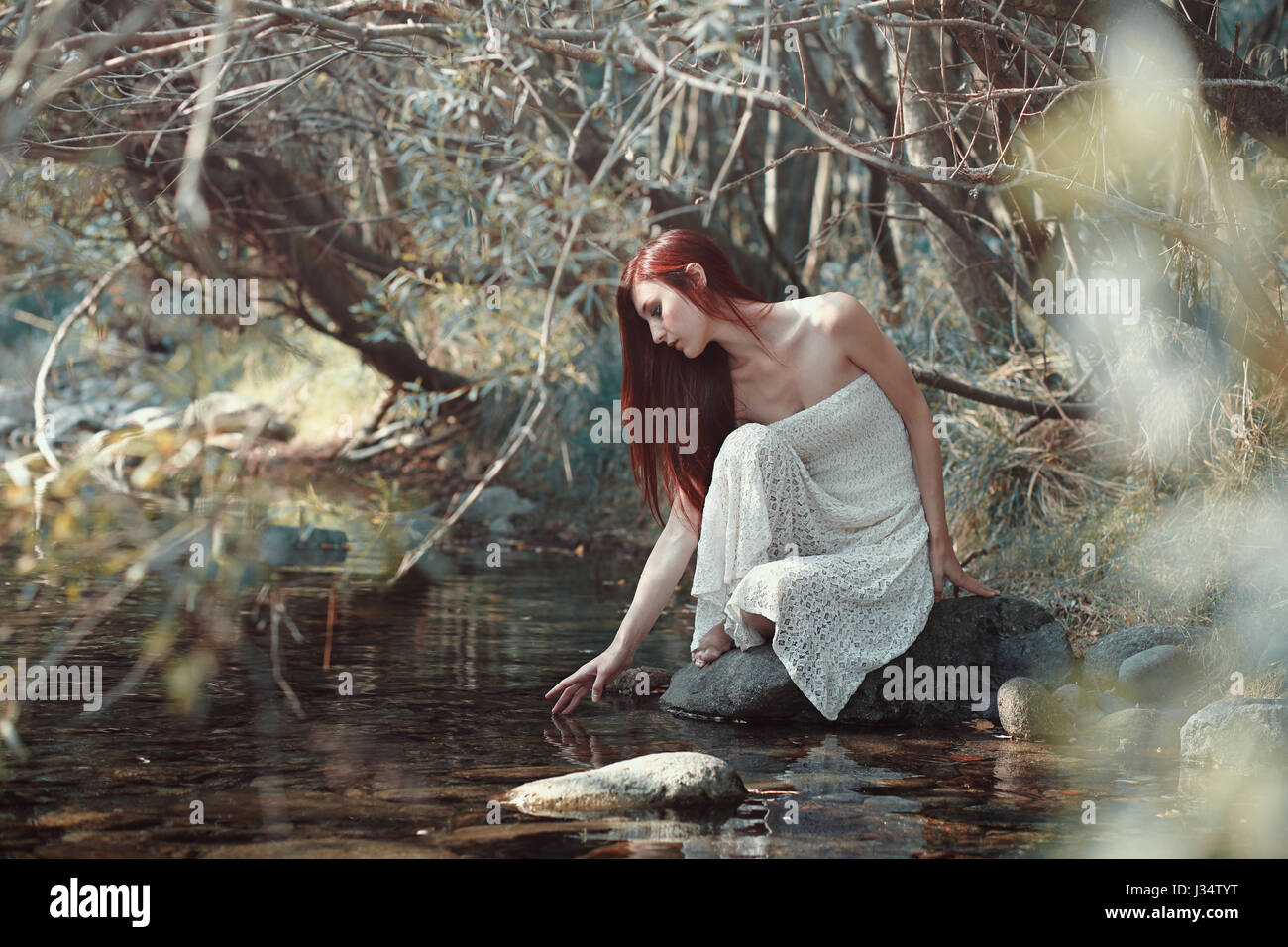 Donna di toccare l'acqua in un flusso. Sunny boschi Foto Stock