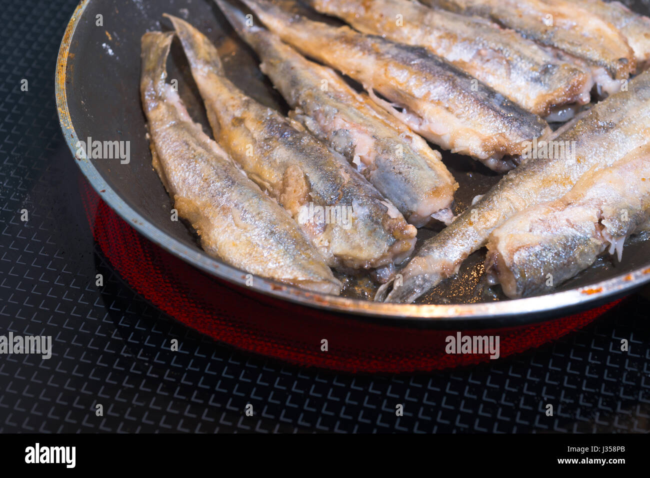 In parte nutriente pesce di mare Capelin impilati in fila su una padella e stir-fried su un fornello elettrico con un coperchio di vetro. La frittura di pesce - Una prelibatezza Foto Stock