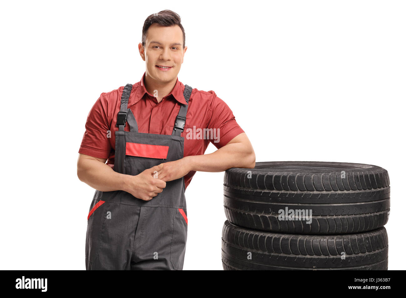 Mechanic appoggiato su una pila di gomme e guardando la telecamera isolata su sfondo bianco Foto Stock