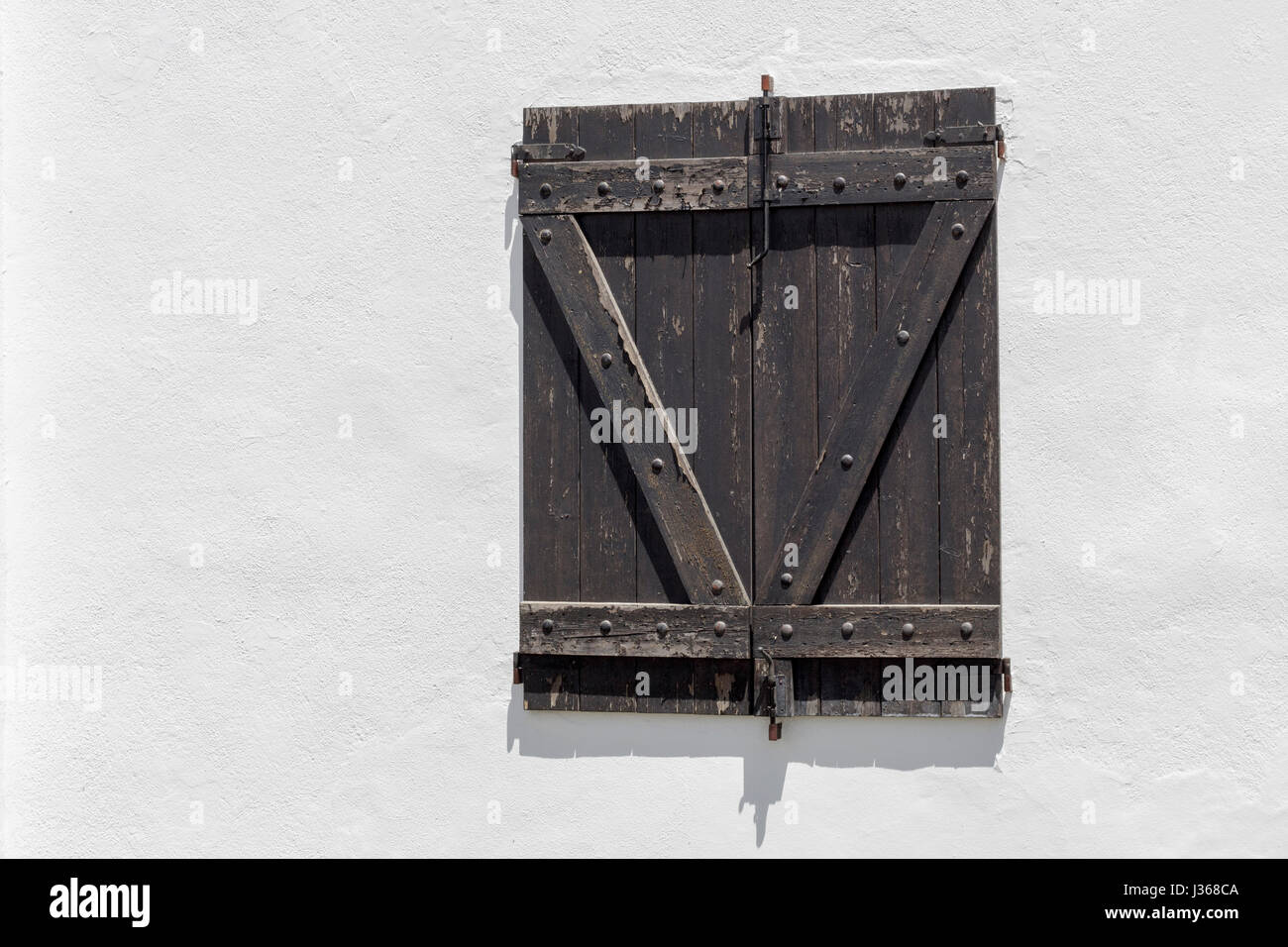 Finestra rustico con stecche di legno scuro su un muro bianco Foto Stock