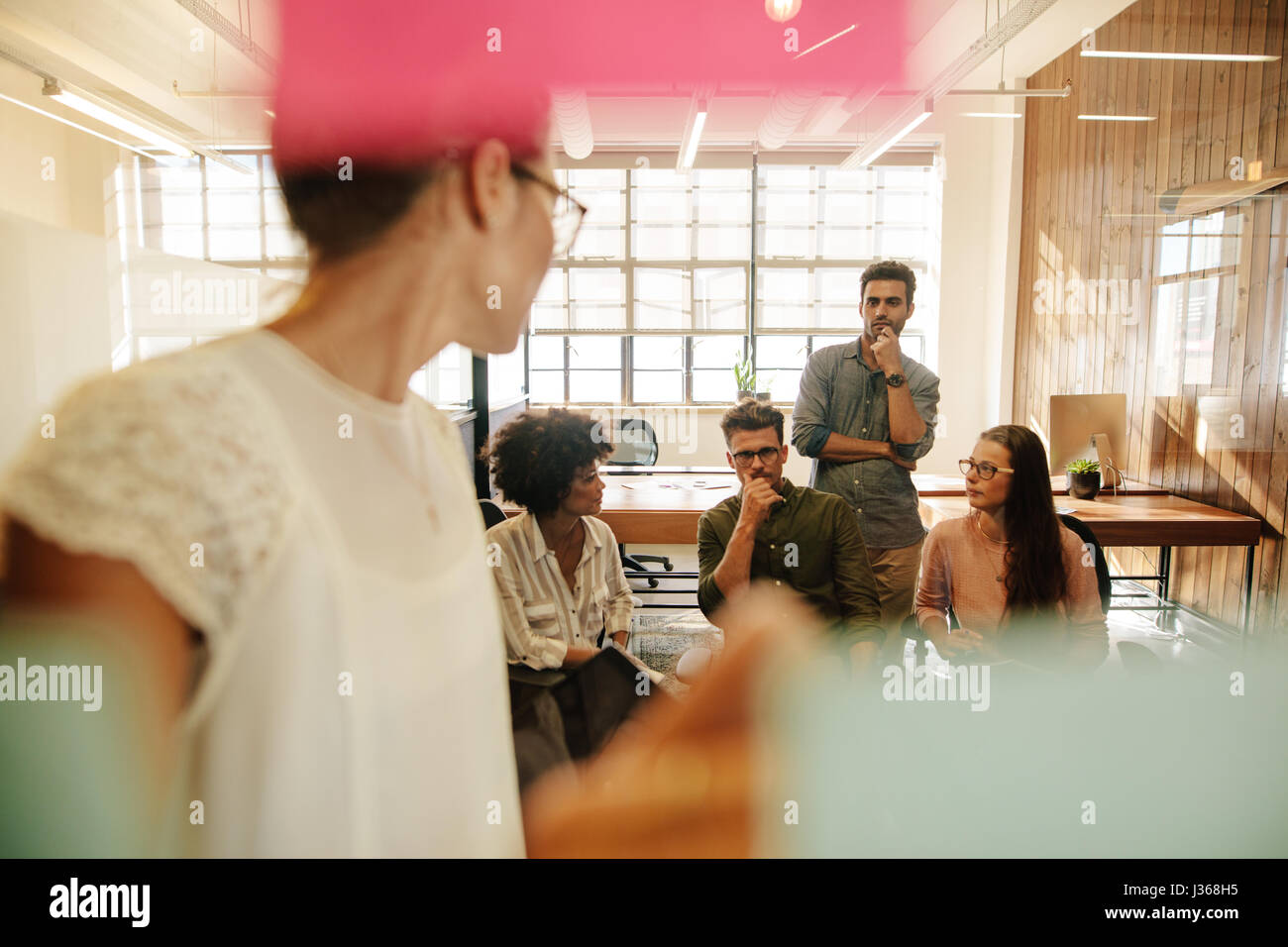 Il team di Business seduti nella sala conferenze con executive femmina in piedi nella parte anteriore della parete di vetro con sticky notes. Foto Stock