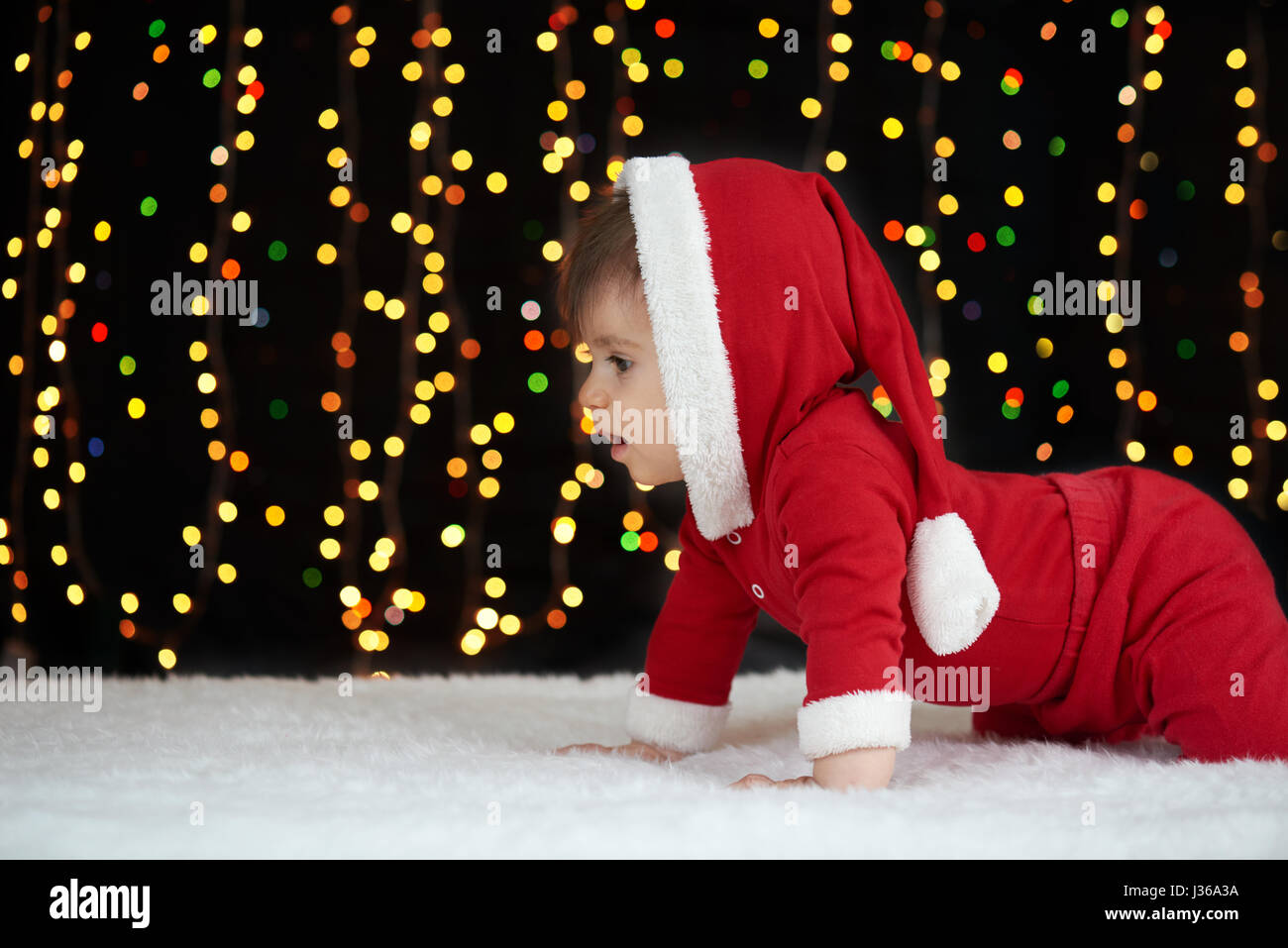 Baby crawl in decorazione di Natale, vestito come Santa, boke luci su sfondo scuro, vacanze inverno concept Foto Stock