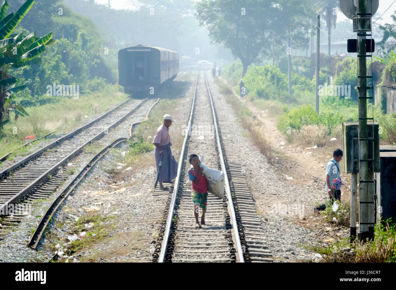 Le persone che attraversano le tracce ferroviarie vicino a un treno, Yangon, Myanmar, Foto Stock