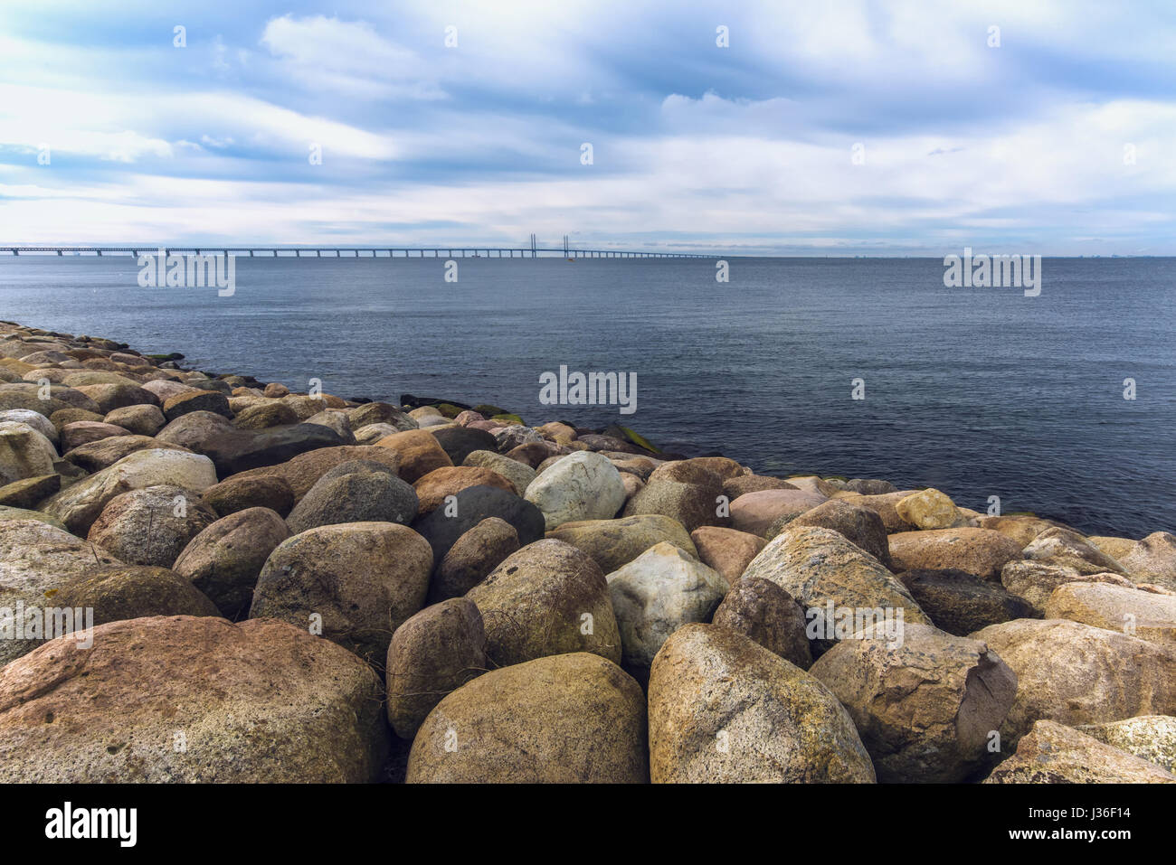 Rocce di grandi dimensioni sulla riva del mare, paesaggi marini e Oresund Bridge in background sulla fredda giornata invernale con drammatica sky Foto Stock