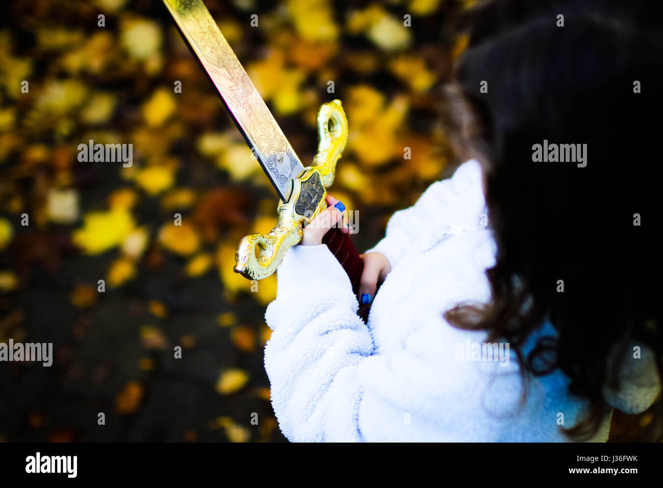 Bambina tenendo una spada dei cavalieri con le sue unghie verniciate e una caduta foglie sfondo. Foto Stock