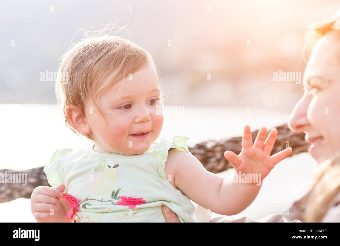 Femmina 1 anni Bambino guarda la sua madre al tramonto in italiano seatown Foto Stock