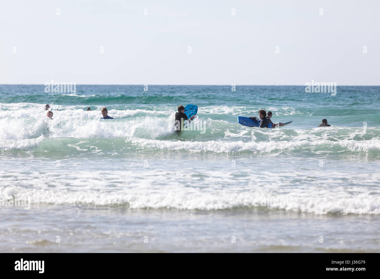 Newquay, Regno Unito. spiaggia frequentatori godetevi il sole in un ambiente luminoso e soleggiato nel pomeriggio a molla su Fistral Beach in Newquay. Giovani surfisti schede del corpo Foto Stock