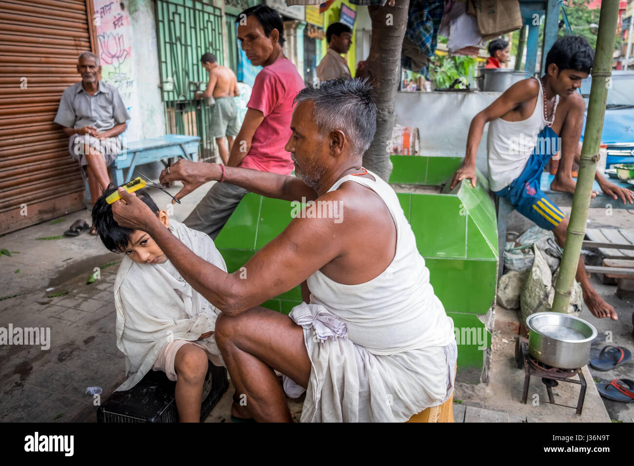 Un uomo di tagliare i capelli a un bambino per le strade di Kumartuli, Kolkata's potters colony Foto Stock