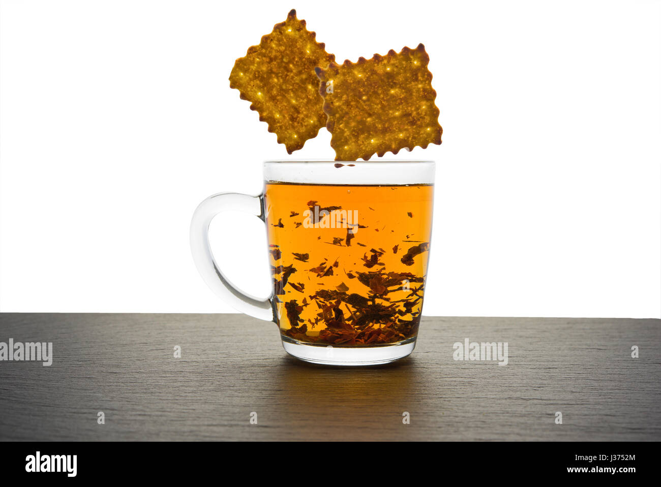Bicchiere di vetro di tè e biscotti in caduta isolato su bianco Foto Stock