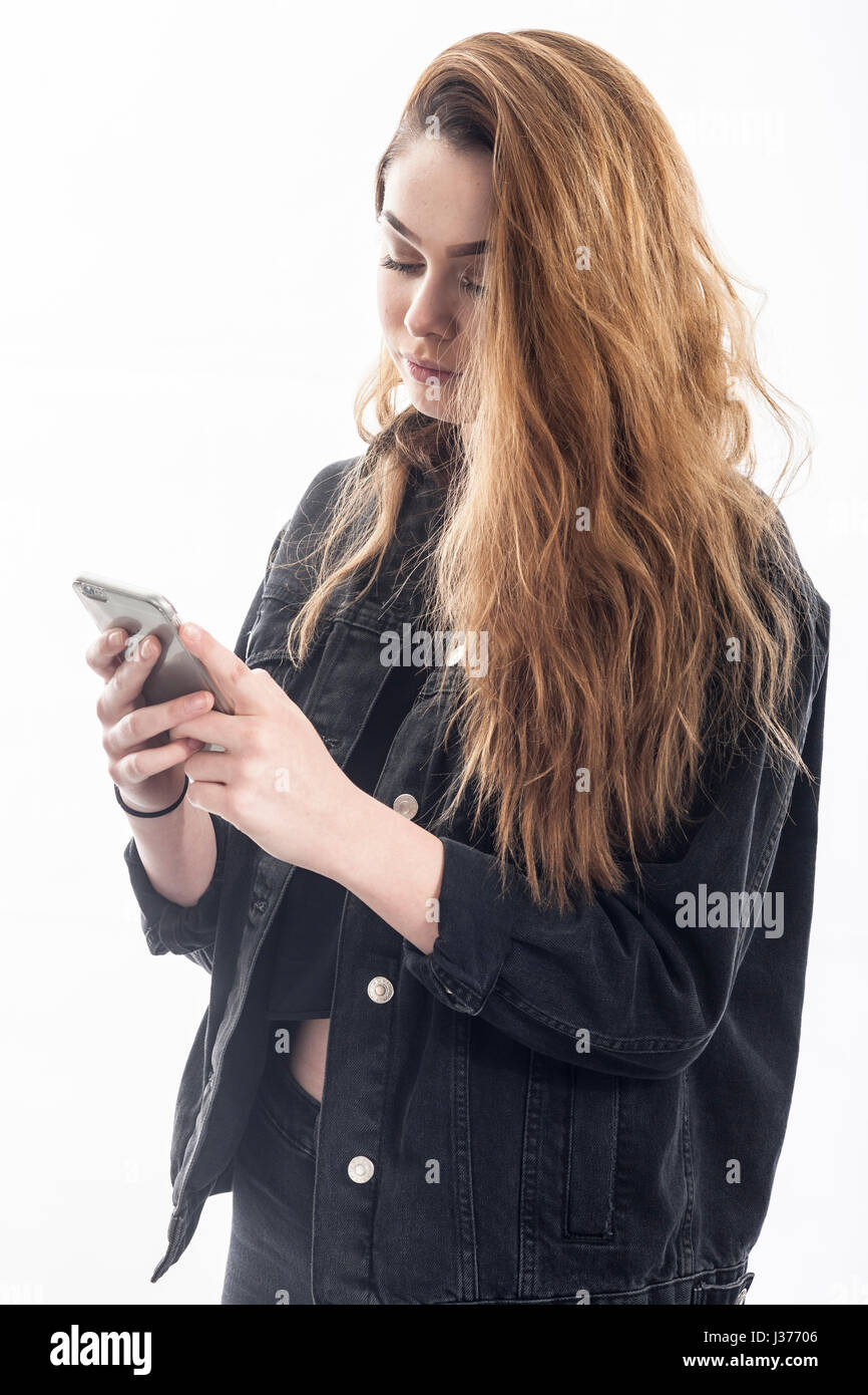 Un grazioso 15 anno vecchia ragazza texting / messaggi sullo smartphone in studio contro uno sfondo bianco nel Regno Unito Foto Stock