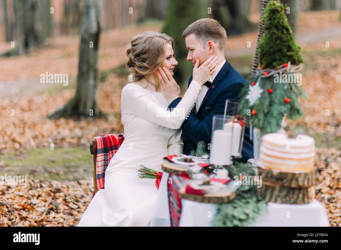 Affascinante coppia di nozze di accarezzare dolcemente la faccia di ogni altra alla tabella di festa nella foresta di autunno Foto Stock