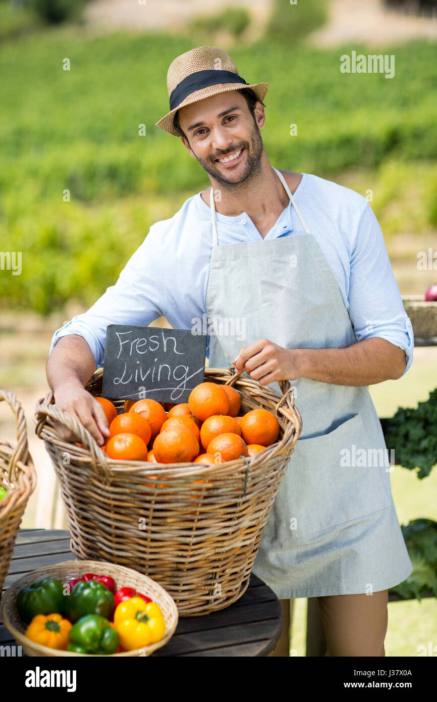 Ritratto di contadino sorridente in piedi da arance fresche nel contenitore al mercato di fattoria per la vendita Foto Stock