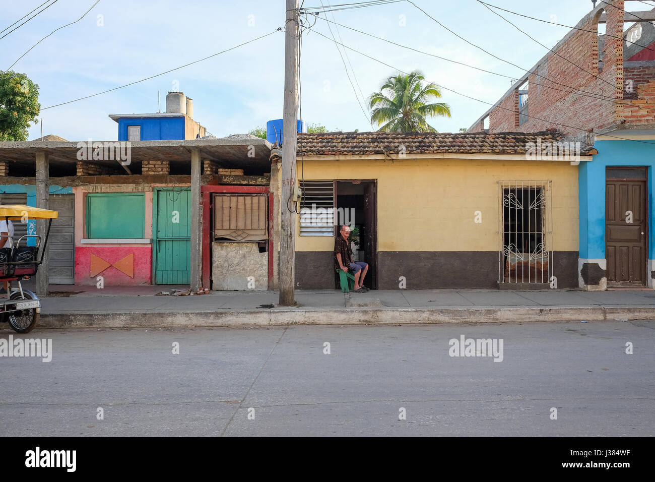 Strada locale vita in Trinidad, Sancti Spiritus, Cuba. Uomo seduto da solo sulla sua porta. Foto Stock