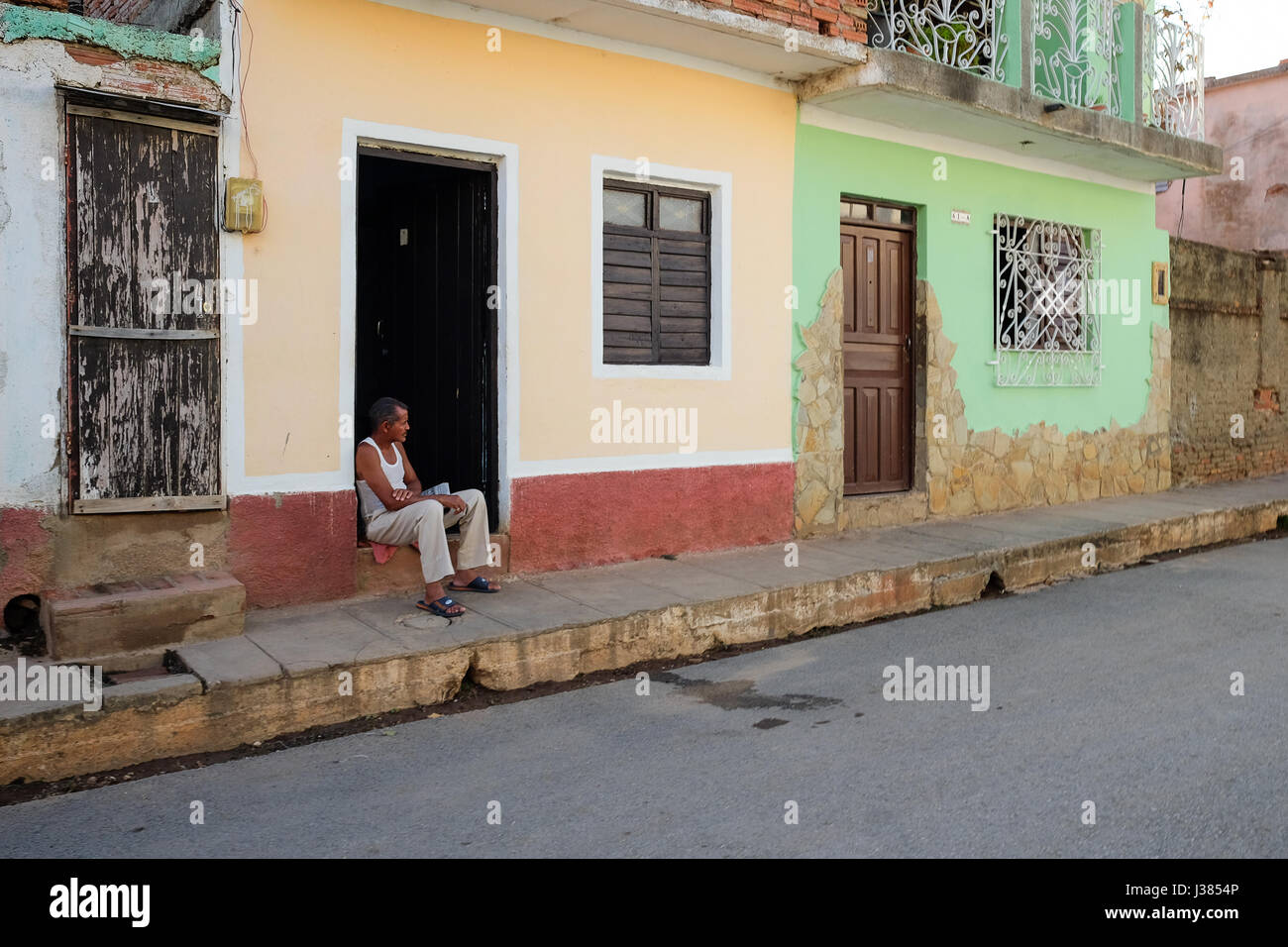 Scena di strada in Trinidad, Sancti Spiritus, Cuba. Cubano locale uomo seduto da solo davanti al suo sbriciolamento home. Foto Stock