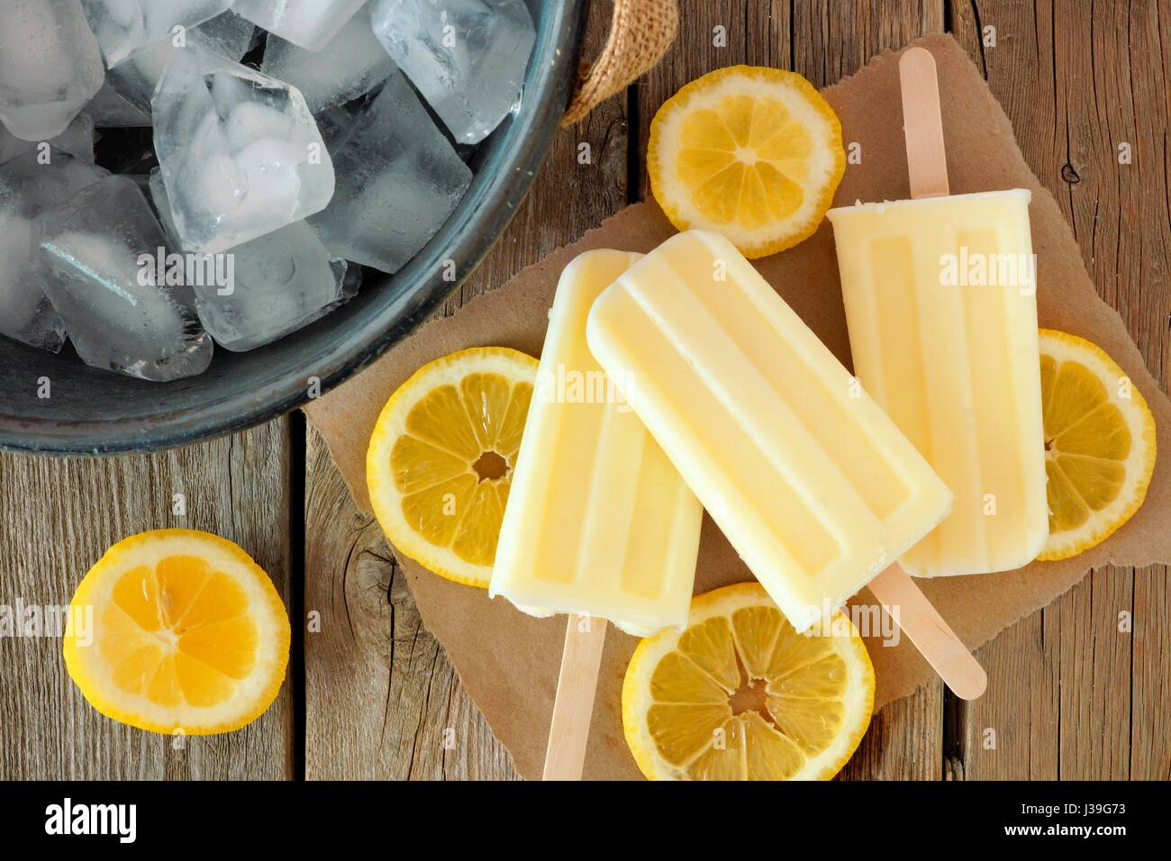In casa di yogurt al limone popsicles con fettine di limone fresco su carta con legno rustico sfondo Foto Stock