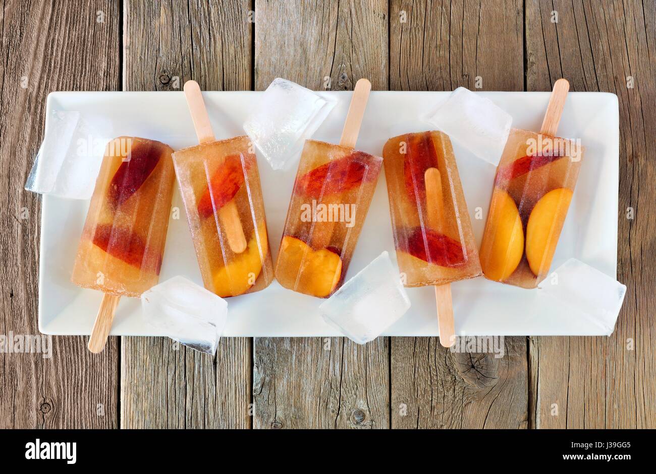 Peach tè freddo popsicles con cubetti di ghiaccio sulla piastra bianca e legno rustico sfondo Foto Stock