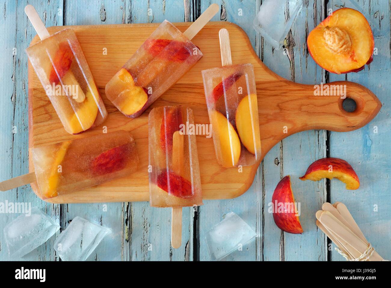 In casa peach tè freddo popsicles, sulla paletta scheda contro rustico in legno blu sullo sfondo Foto Stock