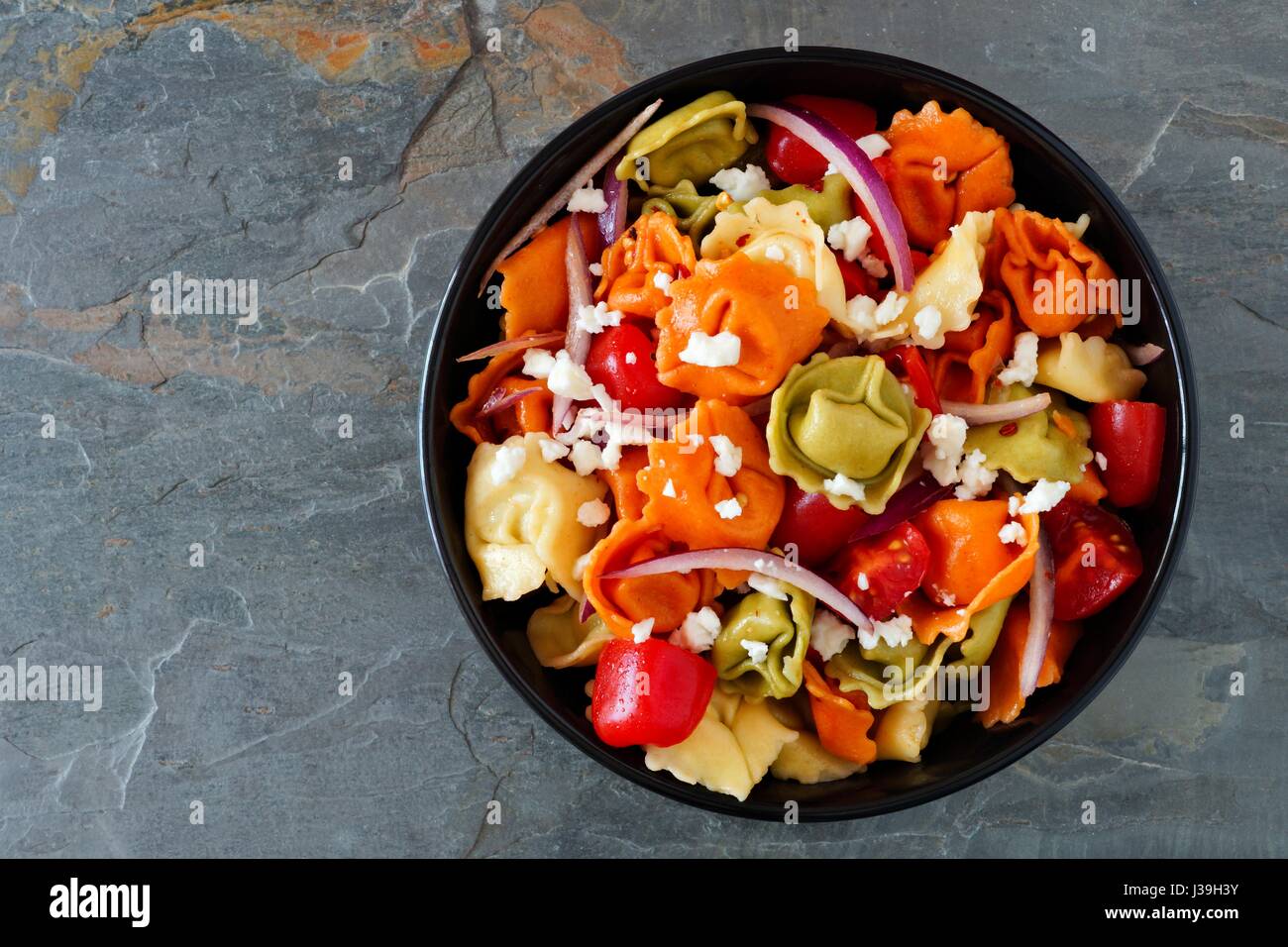 Colorato tortellini con insalata di pomodoro e cipolle, vista aerea al buio su un sfondo di ardesia Foto Stock