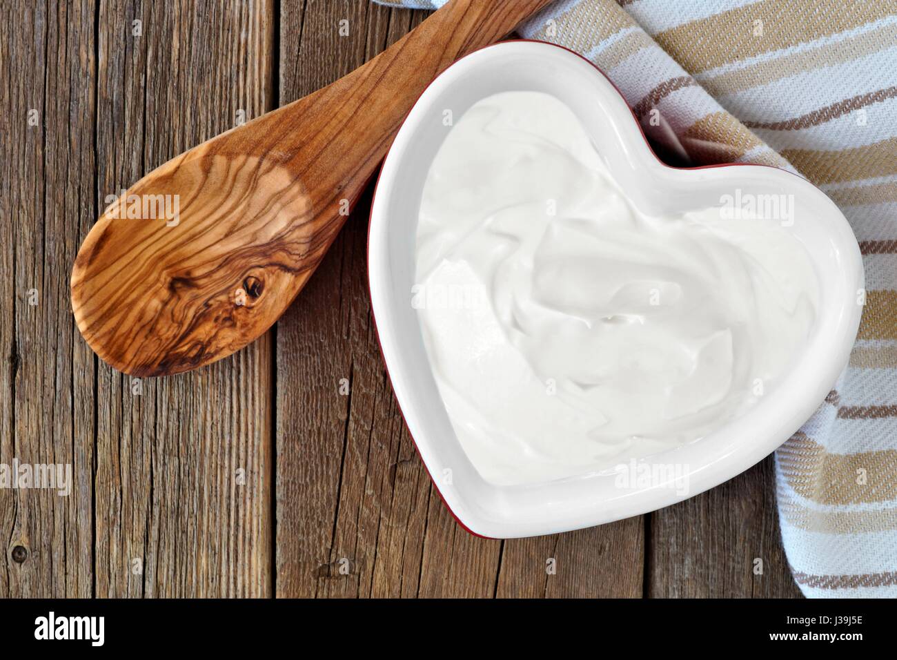 Lo yogurt greco in un cuore ciotola sagomata, overhead scena contro un rustico sfondo legno Foto Stock