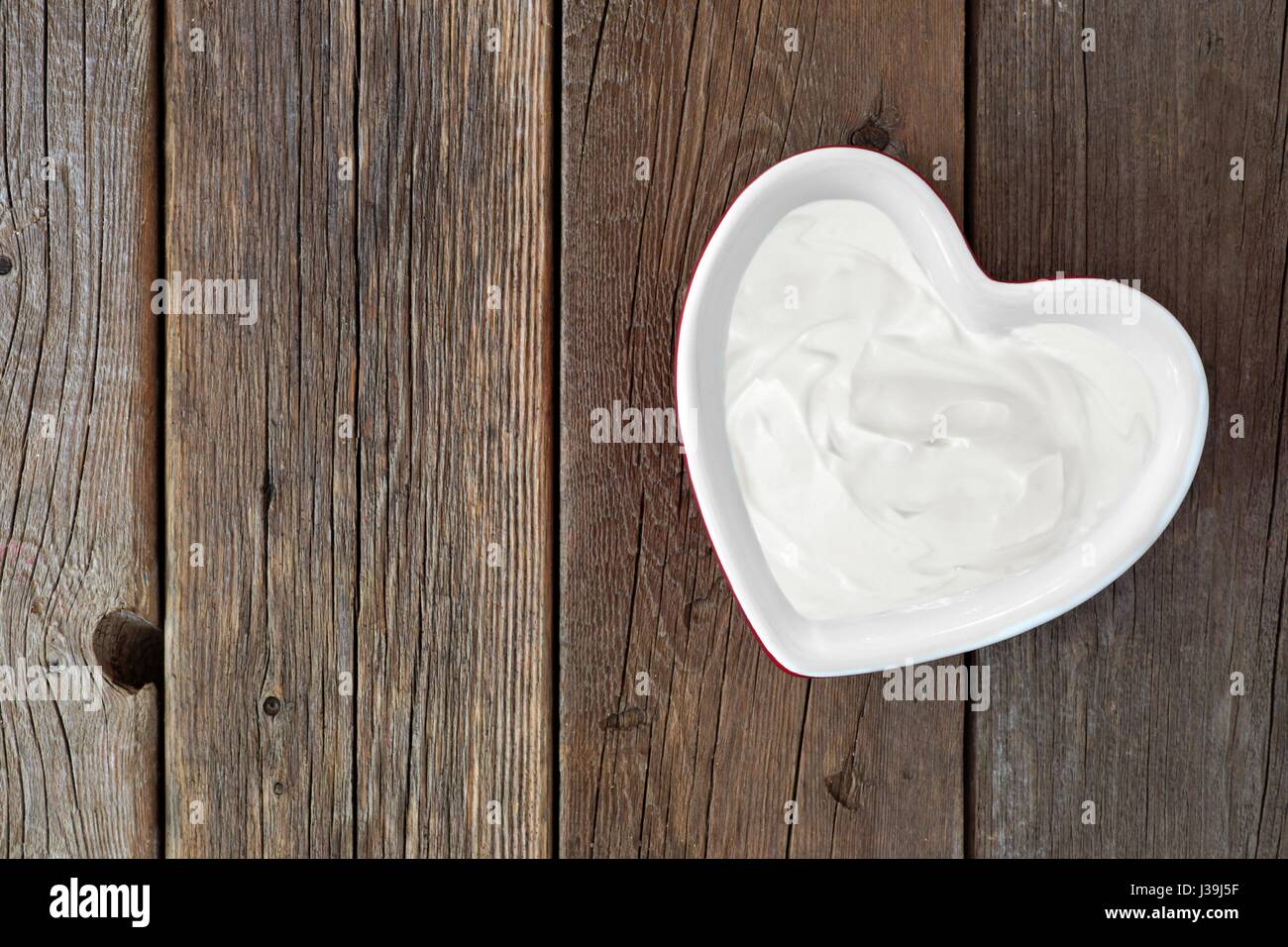 Lo yogurt greco in un cuore ciotola sagomata, vista verso il basso su un rustico sfondo legno Foto Stock