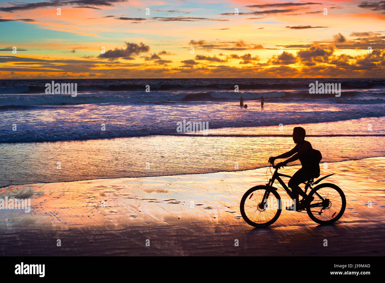 Silhouette di un uomo in sella ad una bicicletta al tramonto sulla spiaggia. Isola di Bali, Indonesia Foto Stock