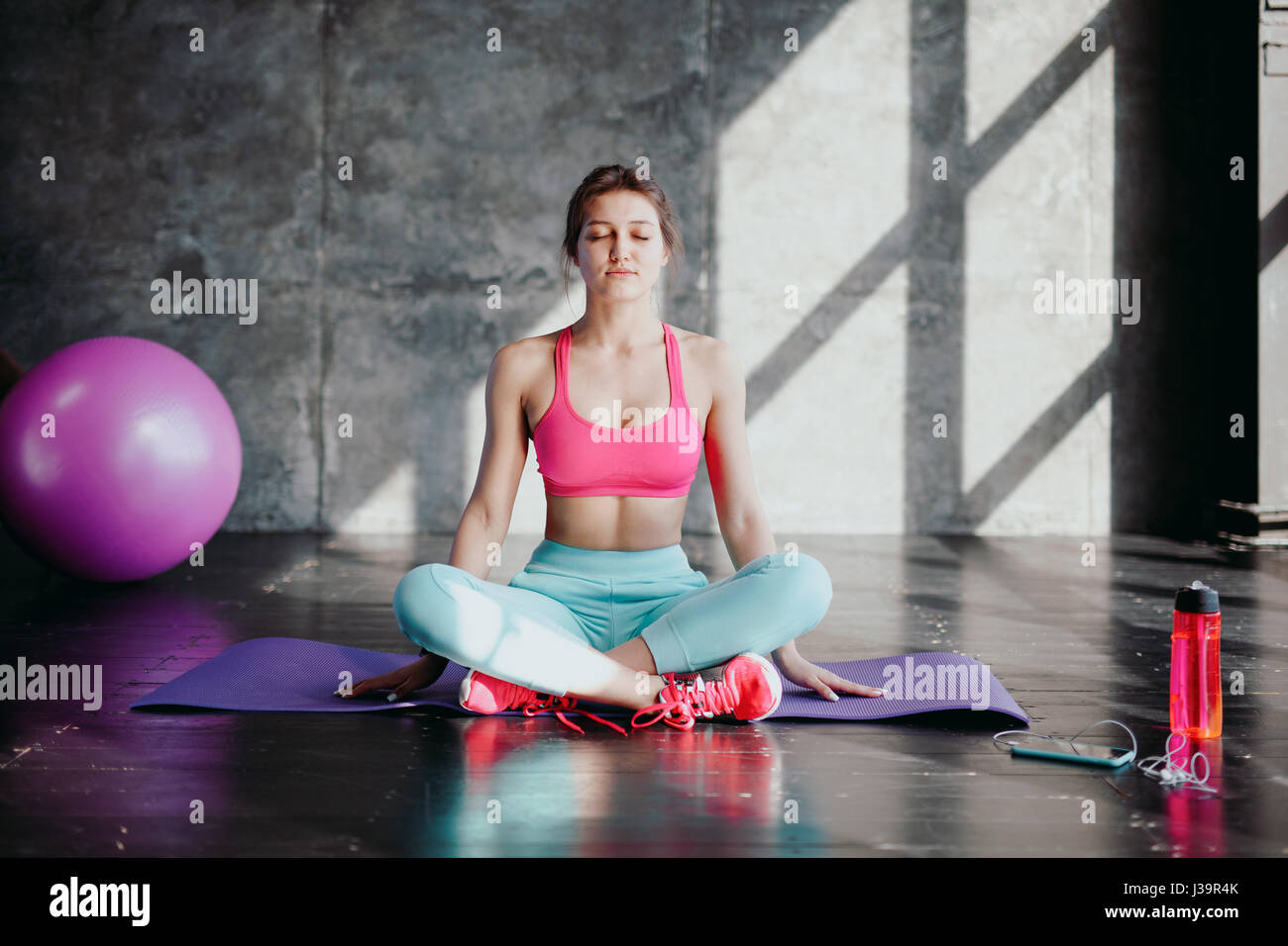 La donna a praticare yoga in lotus pongono indoor. Montare la ragazza di sportswear seduto in Padmasana esercizio, sessione di meditazione del mattino al fitness studio, Foto Stock