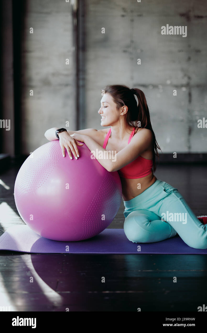 Fitness, sport, formazione e concetto di persone - donna sorridente flessione dei muscoli addominali con la palla ginnica in palestra Foto Stock
