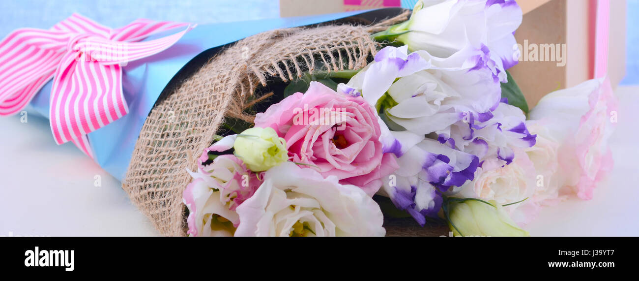La festa della mamma lisianthus fiori avvolto in tela e carta blu con scatola regalo bianca sul tavolo di legno e sfondo blu è dimensionato per adattarsi un popolare social m Foto Stock