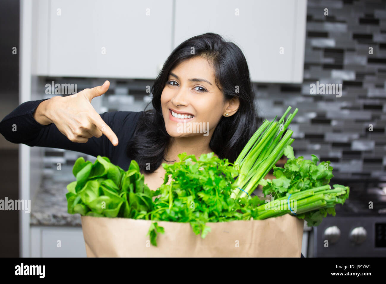Closeup Ritratto, giovane donna che puntano a sacchetto pieno di verde di generi alimentari sani e nutriente dieta bilanciata, isolato in interni home background. Sou localmente Foto Stock