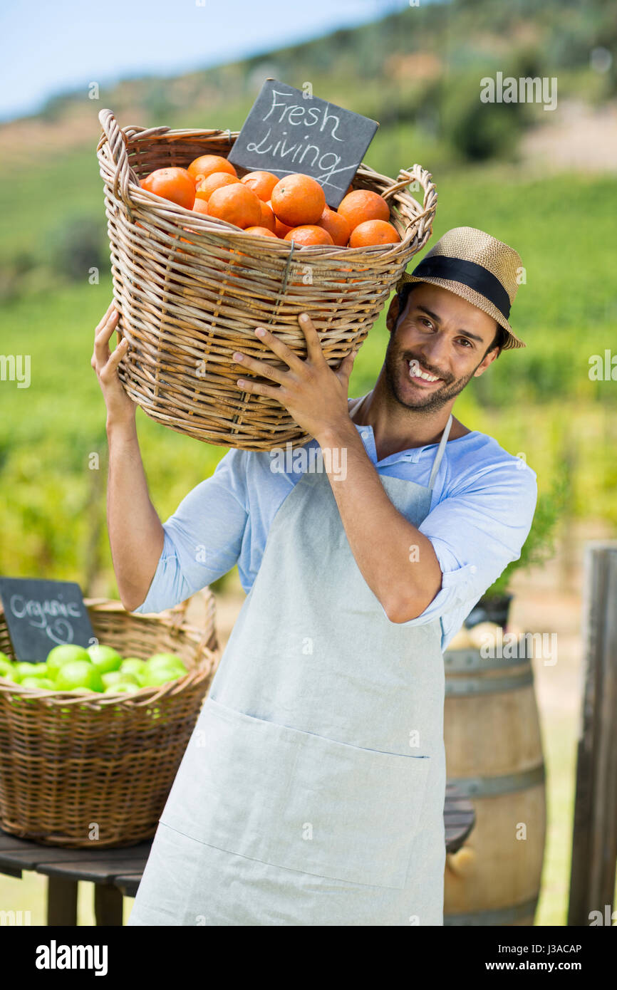 Ritratto di felice agricoltore che porta da arance fresche nel contenitore al mercato di fattoria per la vendita Foto Stock