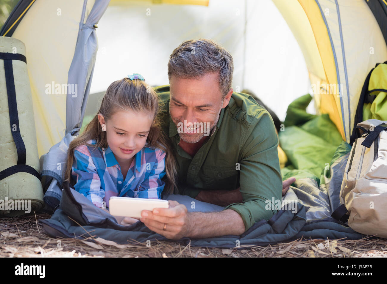 Padre e figlia tramite telefono cellulare durante il riposo in tenda al campeggio Foto Stock