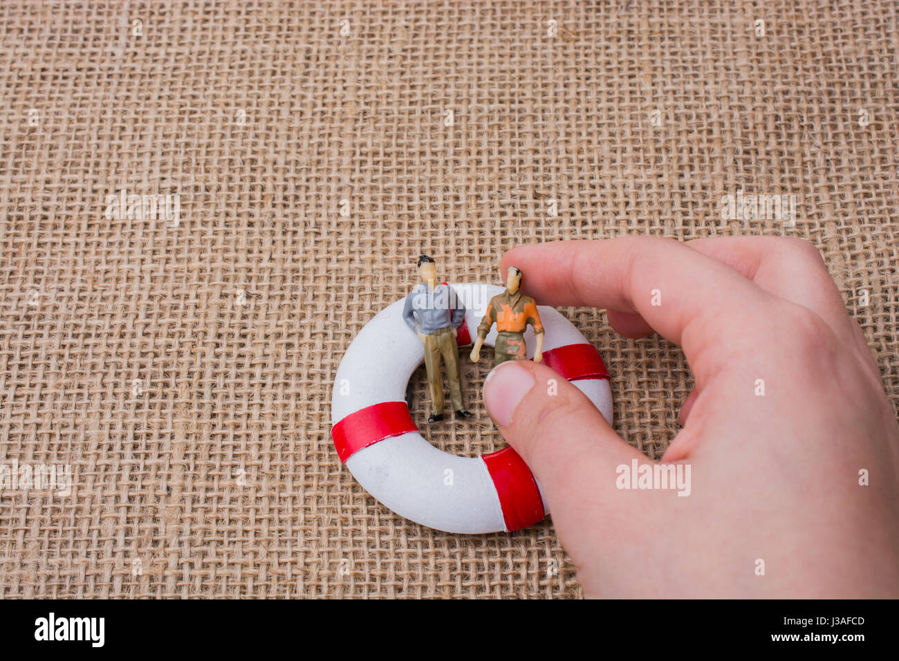 Mano che tiene una figurina uomo in un salvagente sulla vita su tela Foto Stock