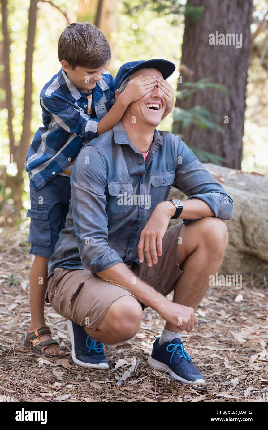 Giocoso ragazzino che copre gli occhi dei padri durante il trekking nella foresta Foto Stock