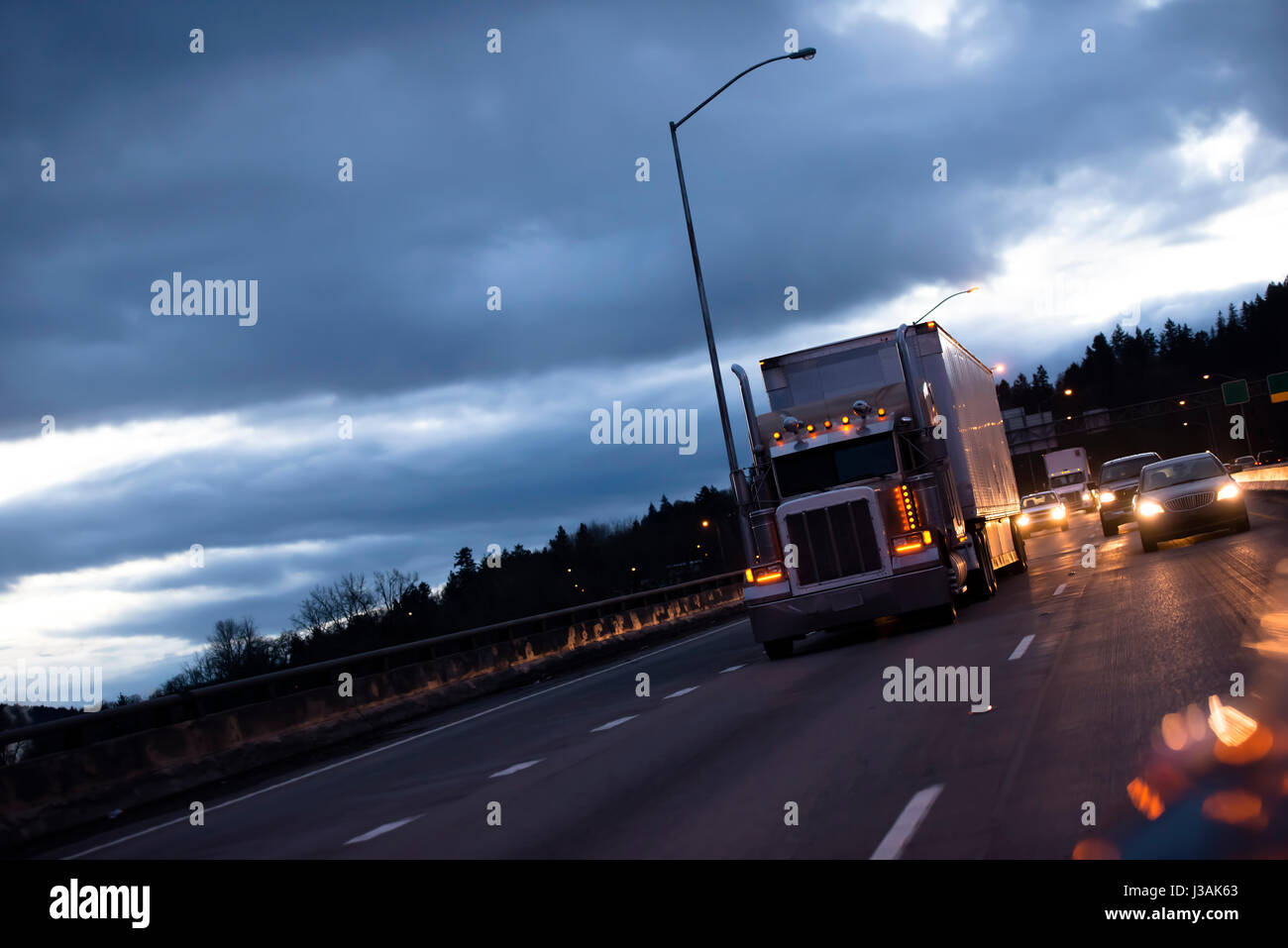 Un classico enorme potente big rig semi carrello con una lunga reefer rimorchio per il trasporto di merci industriali si muove con l'accensione delle luci Foto Stock