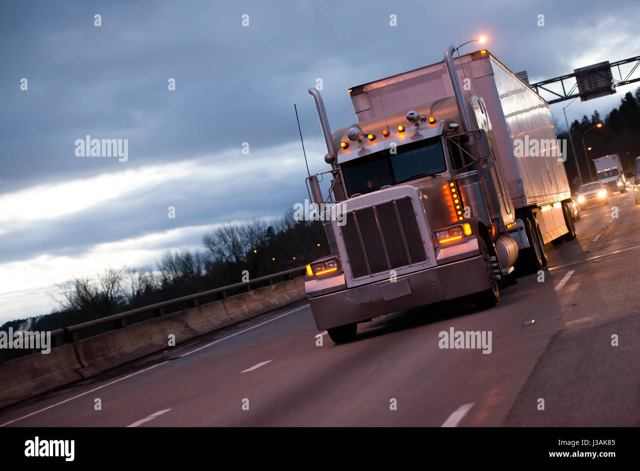Un potente big rig semi carrello con full-sized dry van rimorchio per il trasporto di merci industriali con elevata dei tubi di scarico e un sacco di luci di ingombro Foto Stock