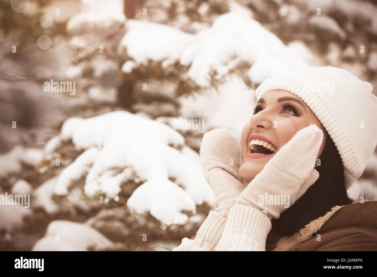 Giovane bella donna in winter park, toccando il suo viso Pelle, ridendo e guardando verso l'alto. Messa a fuoco selettiva, copia spazio, vintage immagine dai toni Foto Stock