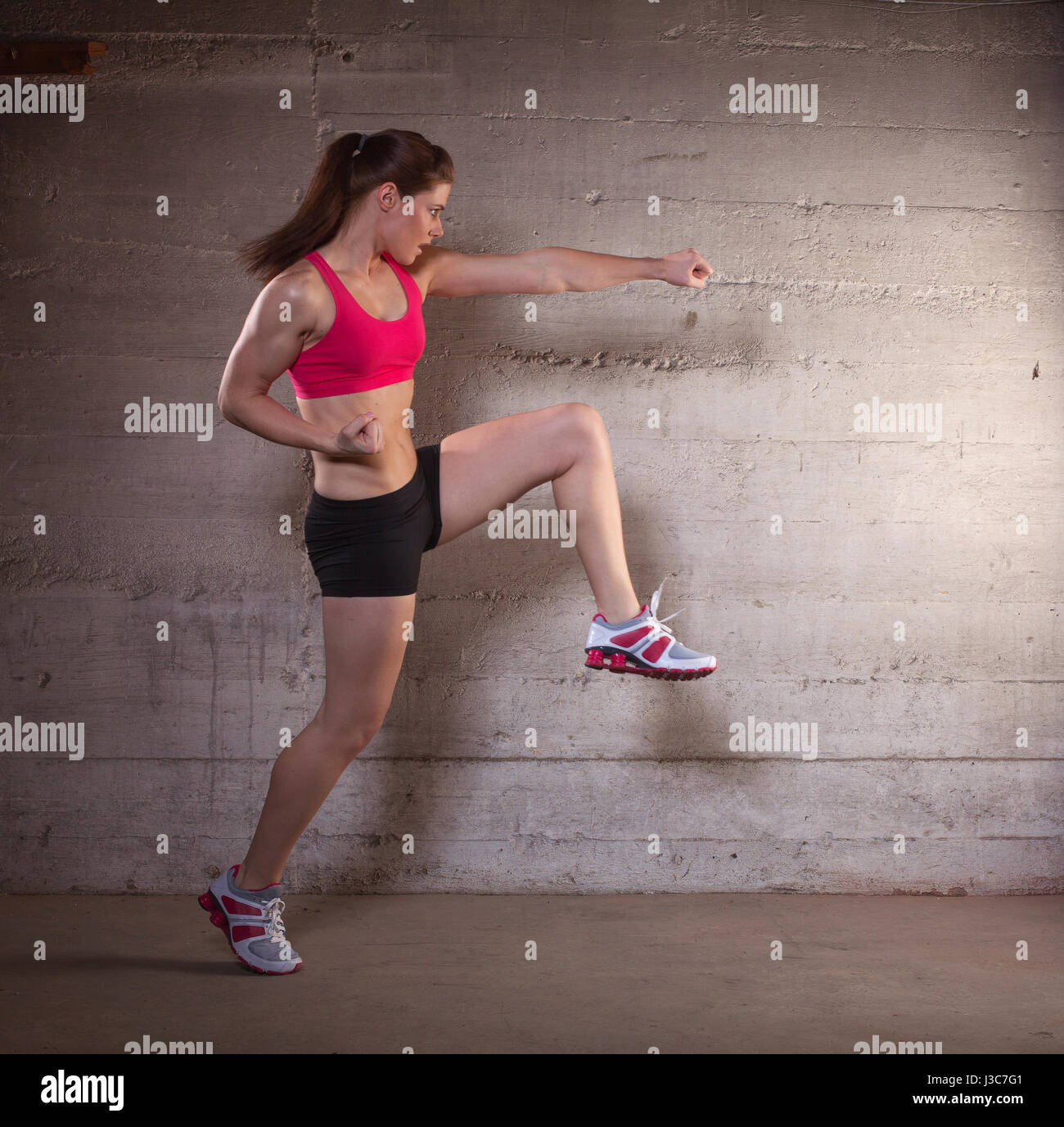 Montare forte donna atletico calci e sferrare pugni. immagine presa dal lato vista. Lei ha le mani avvolto come un lottatore. Foto Stock