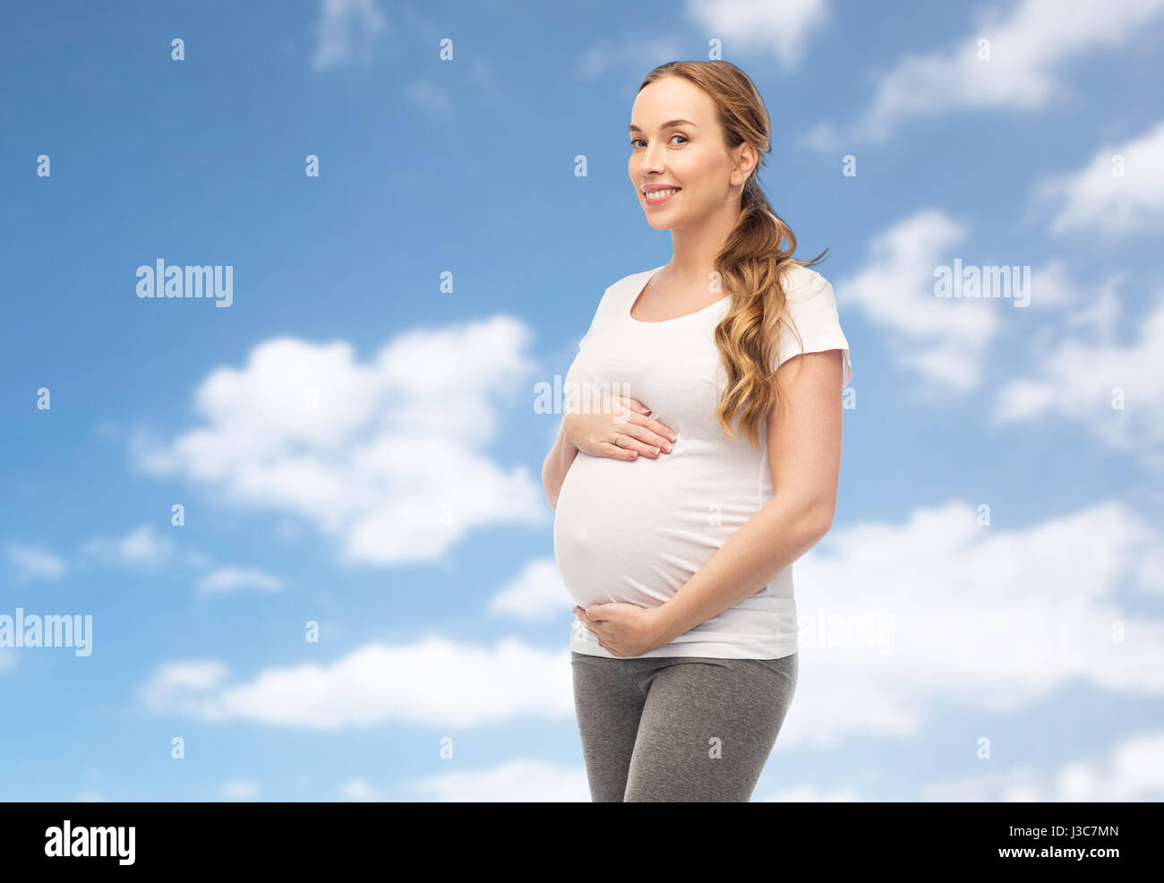 Felice donna incinta toccando il suo ventre su sky Foto Stock
