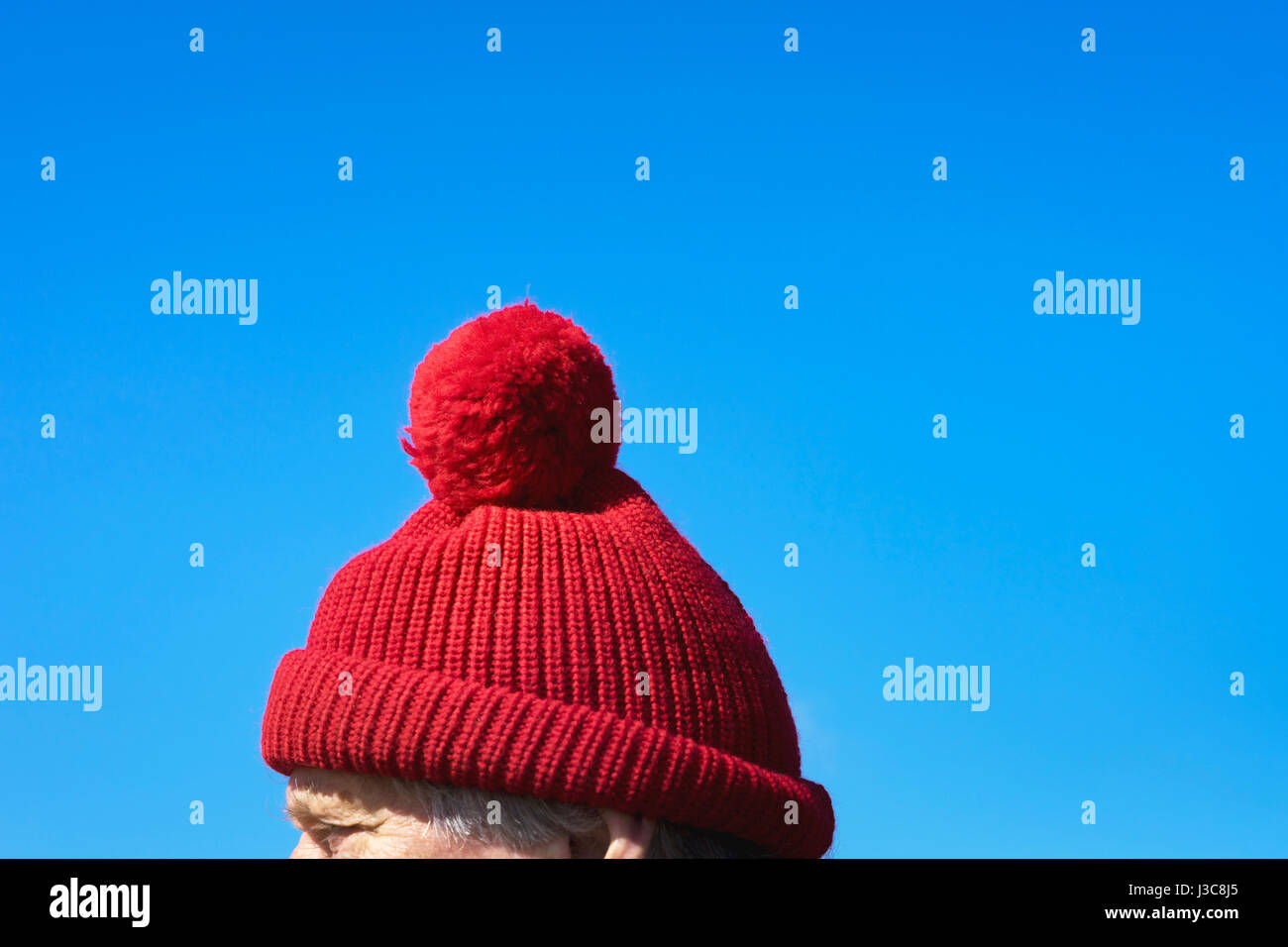 Uomo vecchio con un rosso bobble cappuccio (Pudelmütze) durante la stagione fredda con un luminoso cielo blu sulla piccola Nord Frisia isola Amrum, Germania Foto Stock