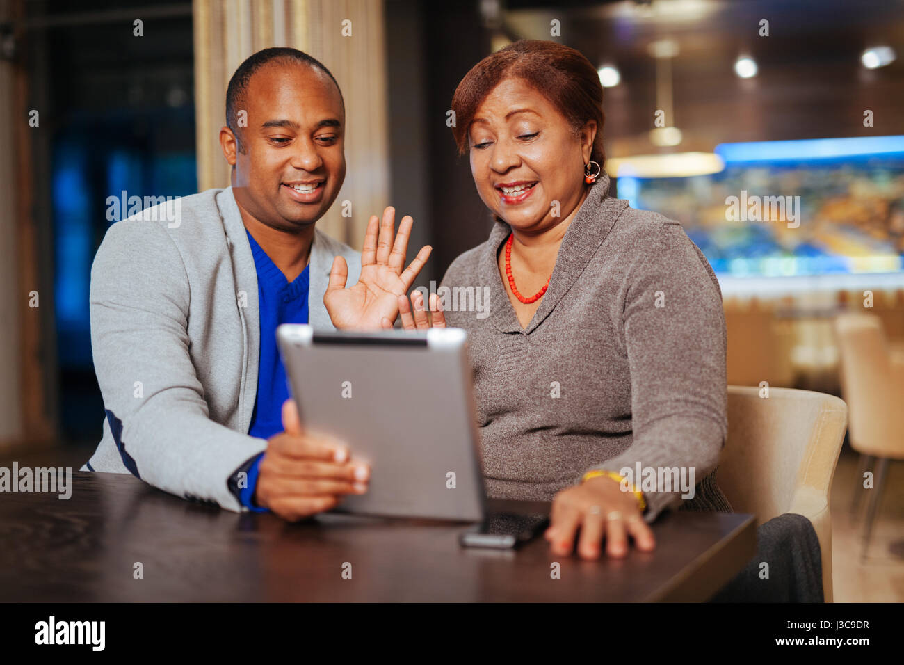 Una madre e figlio di tenere un computer tablet, parlando con gli amici Foto Stock