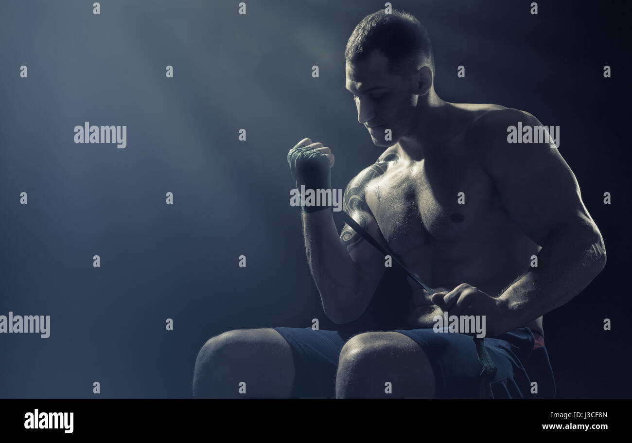 Boxer mettendo su cinghie preparando per combattere su sfondo scuro Foto Stock