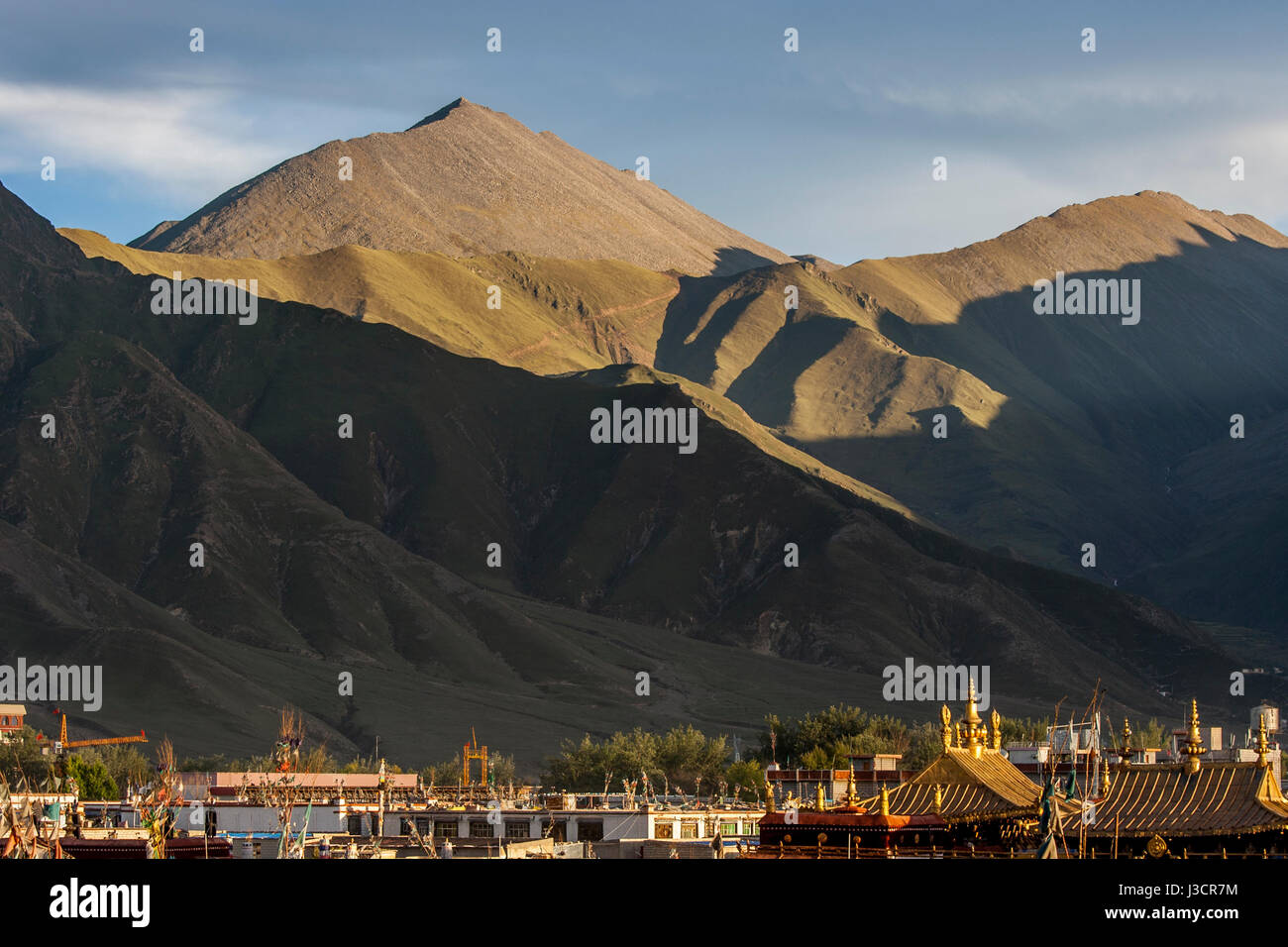 Golden pinnacoli di Jokhang Tempio fra un sacco di tetti di case nella città di Lhasa e nel tardo pomeriggio di sole in montagna in backgroud Foto Stock