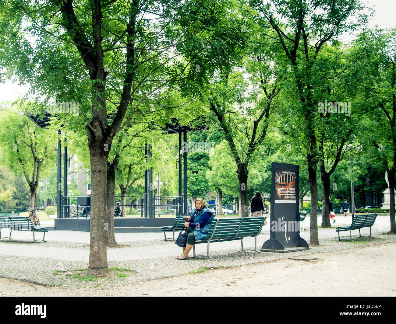 Old Lady est europa immigrato seduto su una panchina di una pubblica piazza Foto Stock