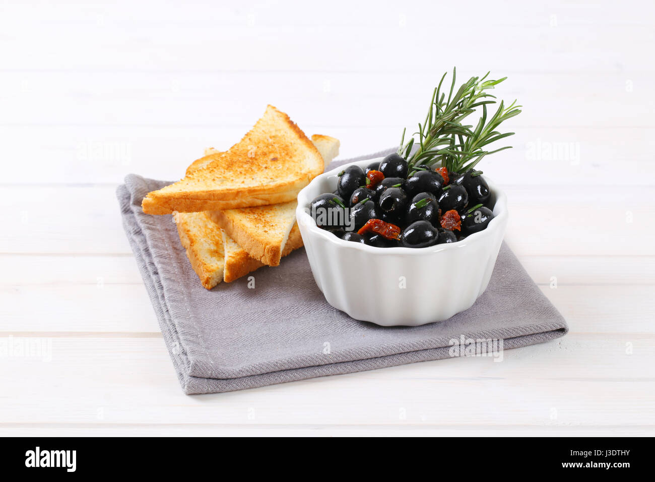 Ciotola di olive nere con pomodori secchi e toast croccanti sul luogo grigio mat Foto Stock