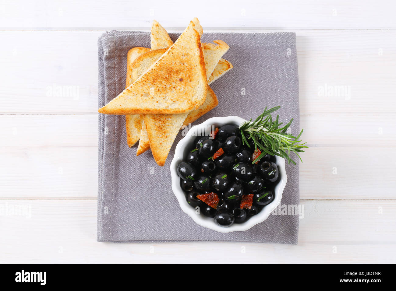 Ciotola di olive nere con pomodori secchi e toast croccanti sul luogo grigio mat Foto Stock