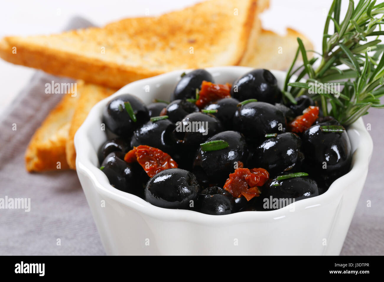 Ciotola di olive nere con pomodori secchi e toast croccanti sul luogo grigio mat - close up Foto Stock