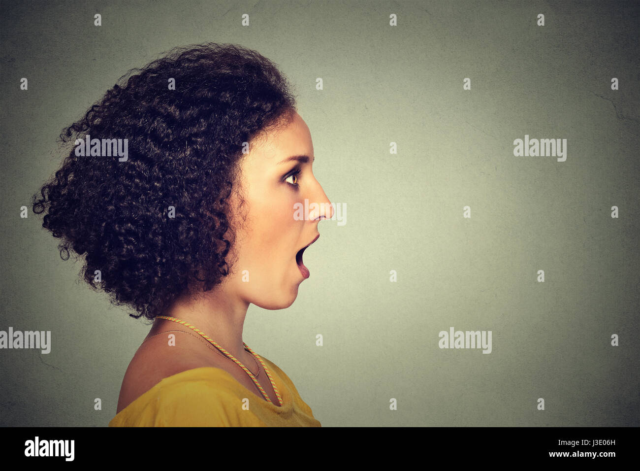 Primo piano vista laterale ritratto di profilo di donna che parla con il suono esce dalla sua bocca aperta isolata parete grigio Sfondo. Volto umano l'espressione delle emozioni Foto Stock